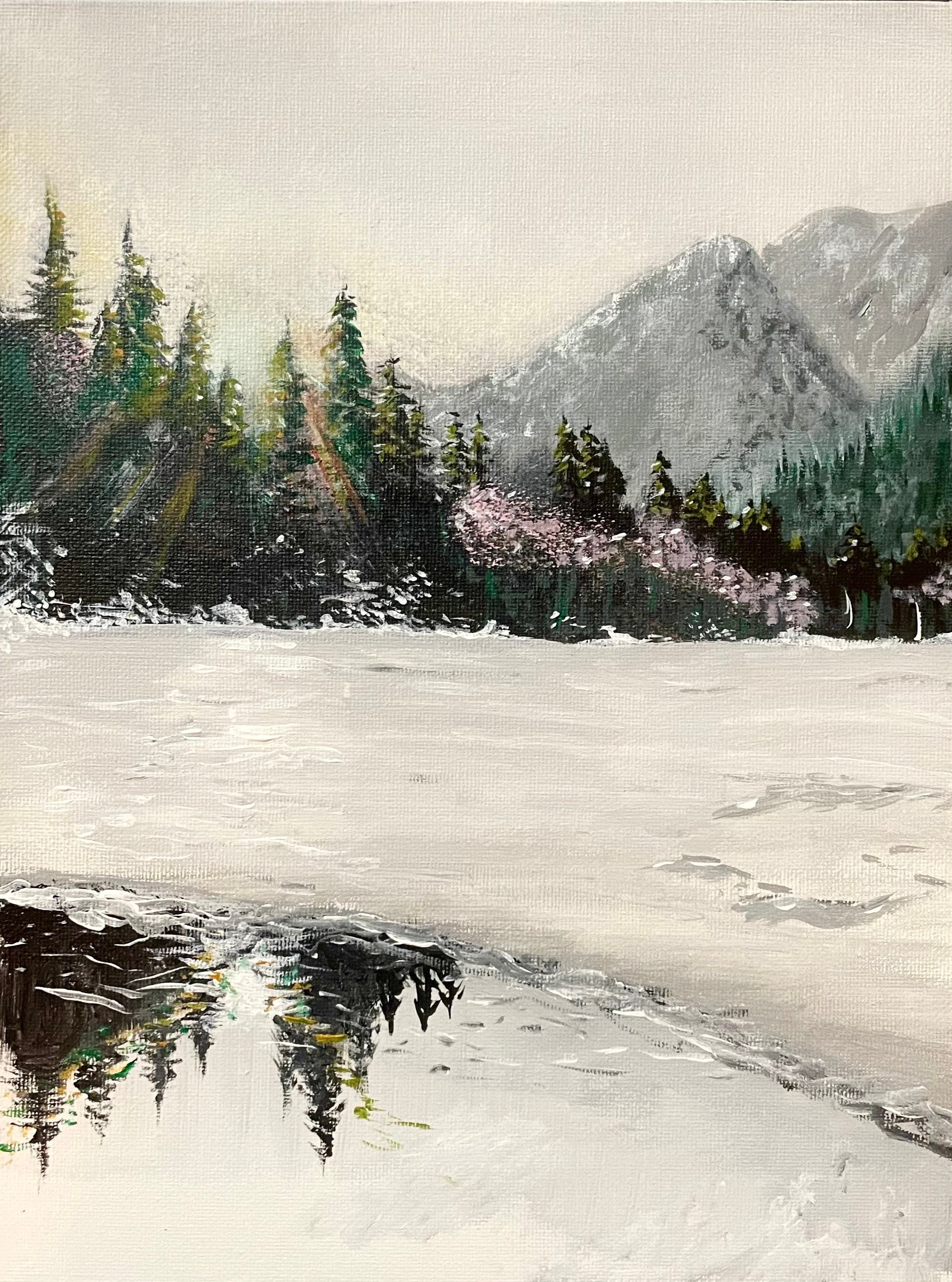 Snowy mountains and evergreens reflect across a lake as sunlight finds its way through the trees.